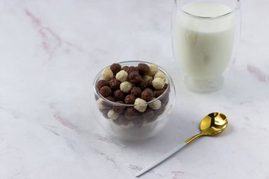 Beyaz arka planda vanilyalı ve çikolata toplu bir kase. Atıştırmalık ve bir bardak süt - hızlı kahvaltı