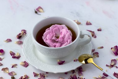 A cup of tea and tea rose petals on a white marble table. Tea ritual