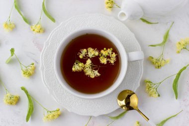 Tea with linden in a white cup on a white marble table. White teapot with aromatic tea. Top view