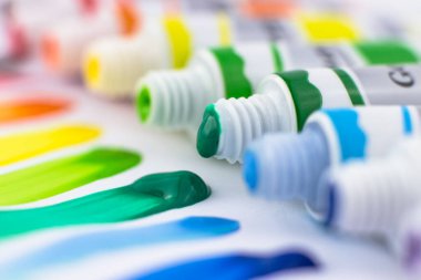 Boya tüpleri ve renkli fırça darbelerinin yakın çekimi. Beyaz arkaplanda boyalar