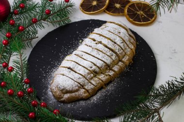 Çalınan parça parça kesilir. Siyah tabakta klasik Alman keki. Tabak Noel ağacı dallarıyla çevrili.