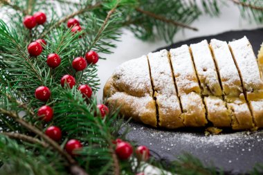 Çalınan parça parça kesilir. Siyah tabakta klasik Alman keki. Tabak Noel ağacı dallarıyla çevrili.