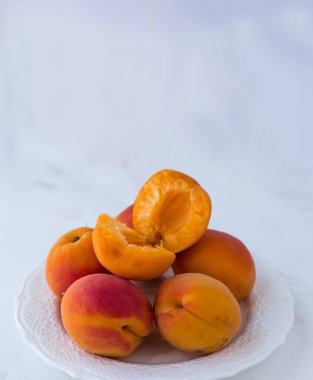 Beyaz bir tabakta sulu olgun kayısılar. Beyaz arka planda yaz meyveleri