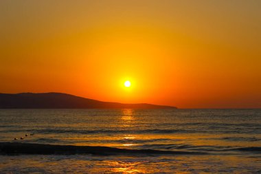 Denizin üzerinde büyüleyici bir gün doğumu. Kırmızı-turuncu gökyüzü ve ufuktaki ilk kuşlar
