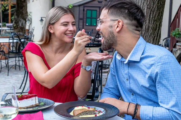 Happy romantic couple feeding each other with desserts after dinner or lunch in a beautiful outdoor restaurant.