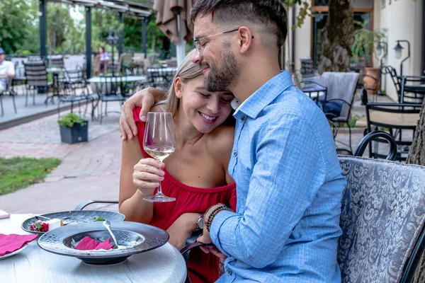 Happy romantic couple hugging and toasting with wine at dinner in a beautiful outdoor restaurant. Lifestyle, love, and relationships.