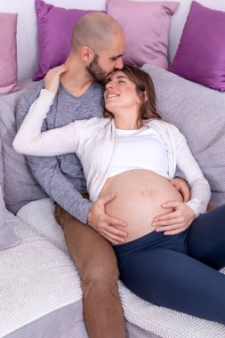 Mutlu bir çift kanepeye uzanmış, çocuk doğurmaya hazırlanıyor. Hamile kadın, eşi tarafından koca göbeğine sarılmıştı..