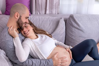 Mutlu bir çift kanepeye uzanmış, çocuk doğurmaya hazırlanıyor. Hamile kadın, eşi tarafından koca göbeğine sarılmıştı..