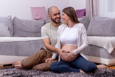 Genç ve mutlu bir çift yerde oturmuş, doğum için hazırlanıyor. Sevgili koca, karısının hamile karnını nazikçe okşar..