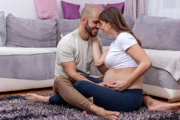 Genç ve mutlu bir çift yerde oturmuş, doğum için hazırlanıyor. Sevgili koca, karısının hamile karnını nazikçe okşar..