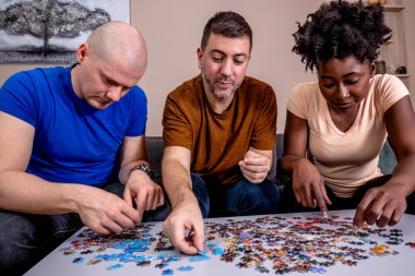 Friends playing jigsaw puzzles at home, on a white wooden table. Putting things together and solving problems. Diversity and fun in a friendship.