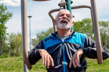 Yorgun bir son sınıf öğrencisi açık havada spor aletleri üzerinde egzersiz yaptıktan sonra soluklanıyor..