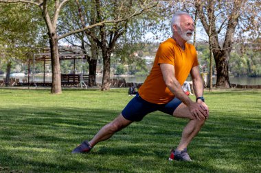 Parkta kararlı bir kıdemli adam egzersizi. Aktif yaşlı erkek bacaklarını açıyor..