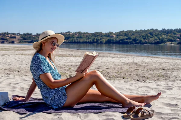 一个戴着太阳镜的年轻貌美的女人正在看书 独自在荒芜的沙滩上消磨时光 — 图库照片