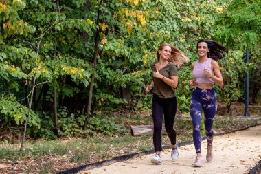 İki kadın koşucu dışarıda aktivitelerini sürdürüyor. Parktaki koşu pistinde koşuyorlar..