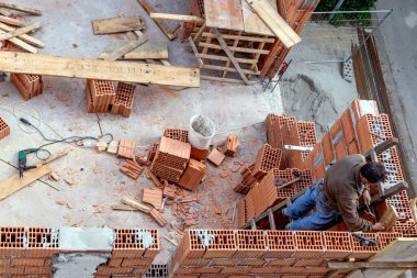 İnşaat işçisi beton ve harçla tuğla duvarlar inşa ederek çalışıyor. Bir duvar ustası yapı taşları ve alçıdan bir ev inşa eder..