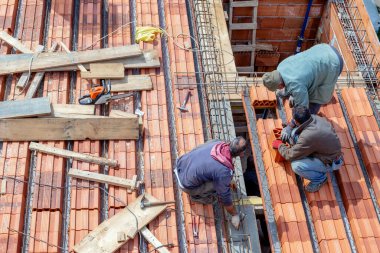 İnşaat işçileri beton dökmeden önce çatı kaplaması uzantısını güçlendirmek için çelik bir ağ hazırlıyorlar..