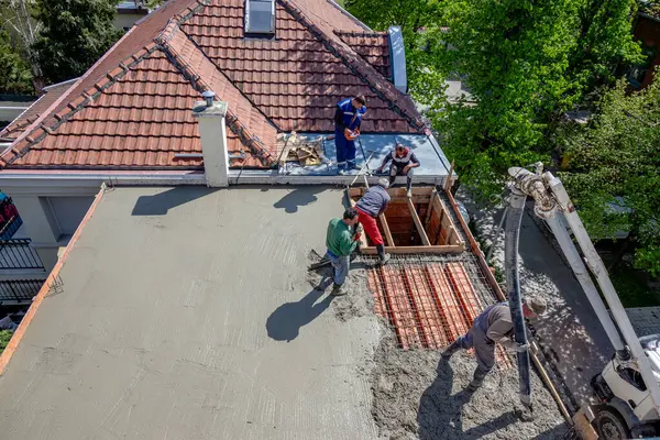 İnşaat işçileri çelik takviyeli çatı levhasına beton karışımı döküyorlar..