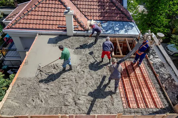 İnşaat işçileri çelik takviyeli çatı levhasına beton karışımı döküyorlar..