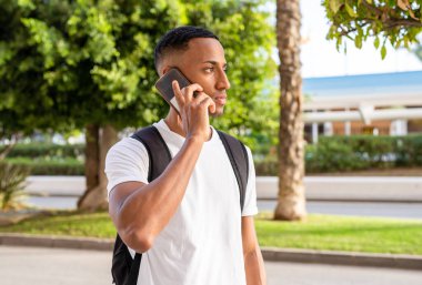 Afro-Amerikalı genç bir adamın gülümsemesi şehrin caddesindeki akıllı telefondan mutlu bir şekilde konuşması..