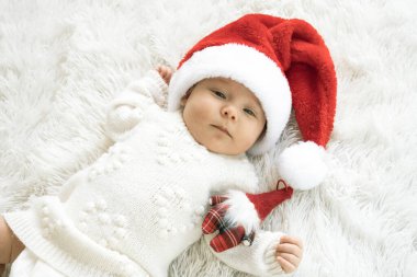 Noel Baba şapkası takan ve küçük sevimli bir kardan adam oyuncağına sarılan yeni doğmuş tatlı bir kızın Noel portresi.