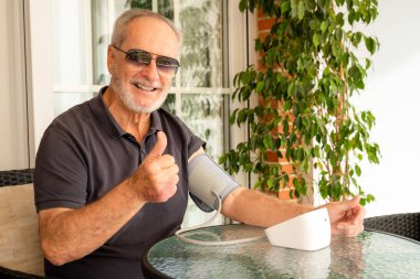 Yaşlılıkta yüksek tansiyon. Atardamar kan basıncını ölçen yaşlı beyaz adam evde terasta oturan koltukta oturan kan basıncı kelepçesini kullanarak tansiyonla ilgili sorunlar yaşıyor. Sağlık ve Tıp Konsepti