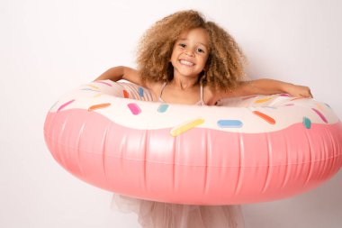 Beyaz tenli, sevimli Afrikalı Amerikalı kız yüzünde renkli lastik bir yüzük tutuyor, yakın, neşeli.