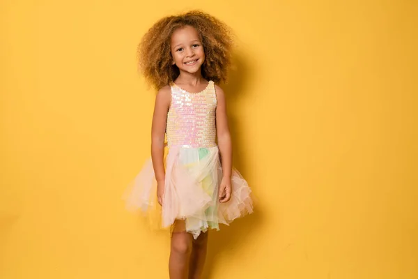 幸せな子供女の子身に着けていますお祝いのドレス立って隔離された上の黄色の背景 — ストック写真