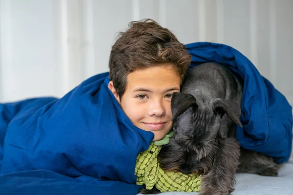 ベッドに横になって犬と一緒にカメラで笑っている幸せな笑顔の子供の男の子 幸せな子供たちの家で楽しい時間を過ごすコンセプト — ストック写真