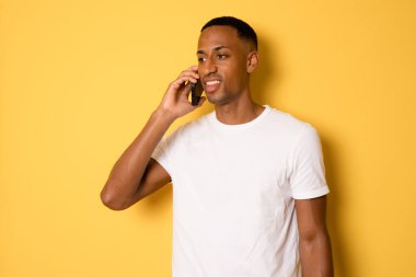 Sarı arka planda izole edilmiş cep telefonuyla konuşan gülümseyen adam..