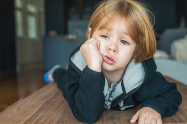 Close up portrait of cute blond child boy with pensive expression at home.