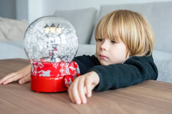 looks at snowy christmas ball, makes a wish to santa for Christmas.