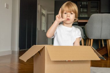 Küçük çocuk yeni evinde karton bir kutuyla eğleniyor..