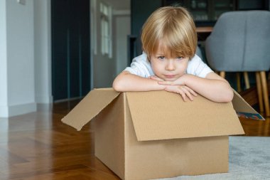 Küçük çocuk yeni evinde karton bir kutuyla eğleniyor..
