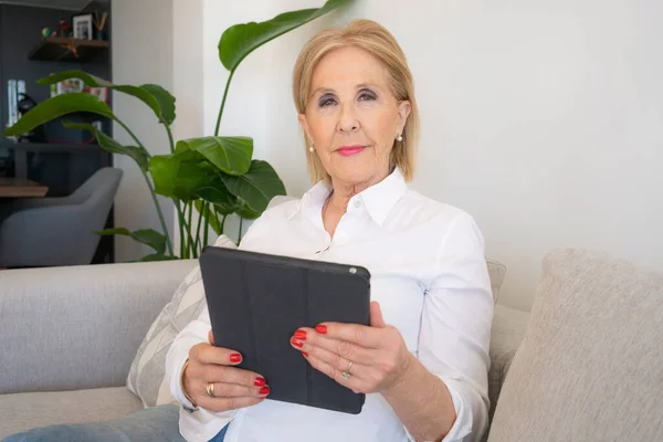 stock image Smiling mature old woman holding using digital tablet relaxing sit on sofa reading e book in reader app, happy middle aged senior grandma browsing internet shopping online on pad computer at home