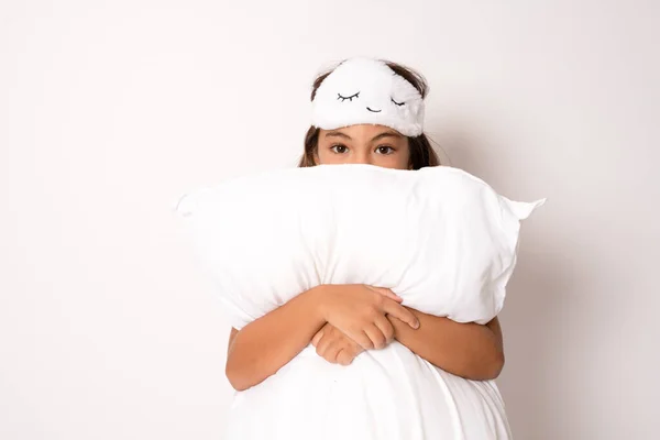 Portrait of positive cheerful sweet kid hug her big soft pillow enjoy weekends free time feel content have bed time wear white sleep-wear isolated over white background