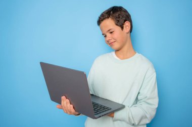 Dizüstü bilgisayar kullanan neşeli çocuğun portresi parlak mavi arka planda izole edilmiş web dersi.