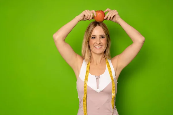 Picture of beautiful young fitness lady standing isolated over green background while holding apple