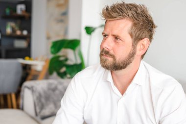 Successful confident young bearded blond adult male entrepreneur businessman professional in business casual clothes sitting at the modern home office and looking at camera
