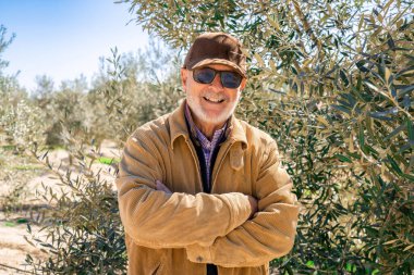 Elderly man smiling with arms folded outdoors in nature looking to camera.