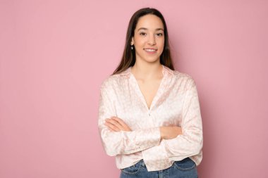 Kollarını katlamış pembe bir arka planda duran mutlu bir kadının portresi.