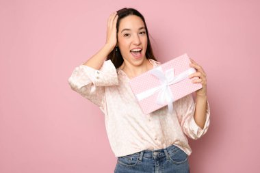 Close-up portrait of happy exited pretty brunette woman holding gift box, looking at camera, isolated on pink background