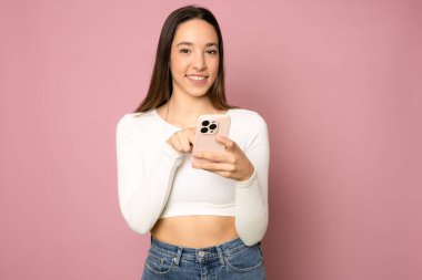 Gülümseyen sıradan bir kadının portresi pembe arka planda akıllı telefonu tutuyor.