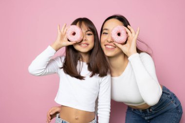 İki kız yeni pişmiş donut kullanarak komik şakalar ve neşeli ifadeler yapıyor.