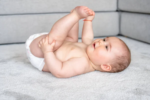 Horizontal profile shot of a jubilant baby girl lying on floor with legs up in the air