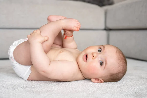 Horizontal profile shot of a jubilant baby girl lying on floor with legs up in the air smiles at the camera.