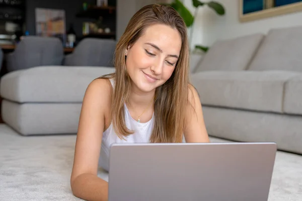 Stock image Happy young woman using laptop lying on carpet at home