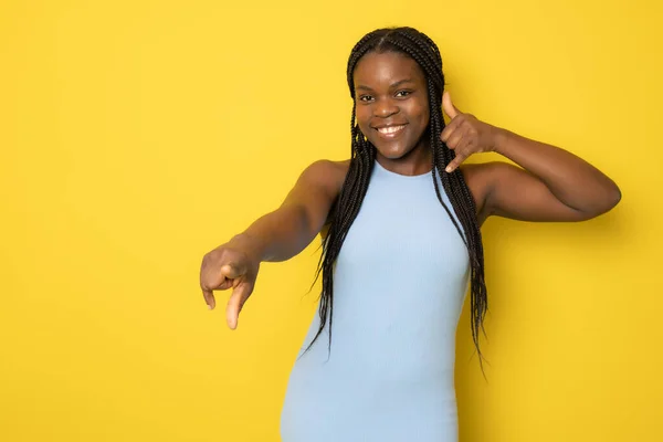 Photo of happy young african lady in casual clothing standing isolated over yellow background. Looking camera while pointing to you.