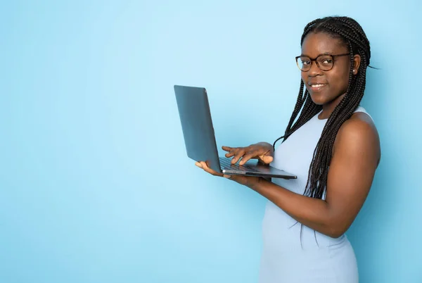 Young smiling black woman standing with laptop computer isolated on blue background