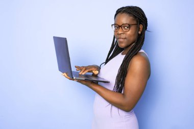 Çekici genç Afrikalı Amerikalı kadın, yüksek teknolojili elektronik cihazını kullanarak açık mor arka planda izole edilmiş eğitimine yardım ediyor.
